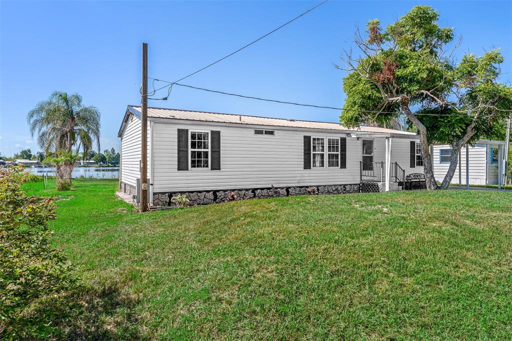 A white mobile home sits on a grassy lot near a body of water — 2008 LAKE ELLEN DRIVE, HAINES CITY, FL