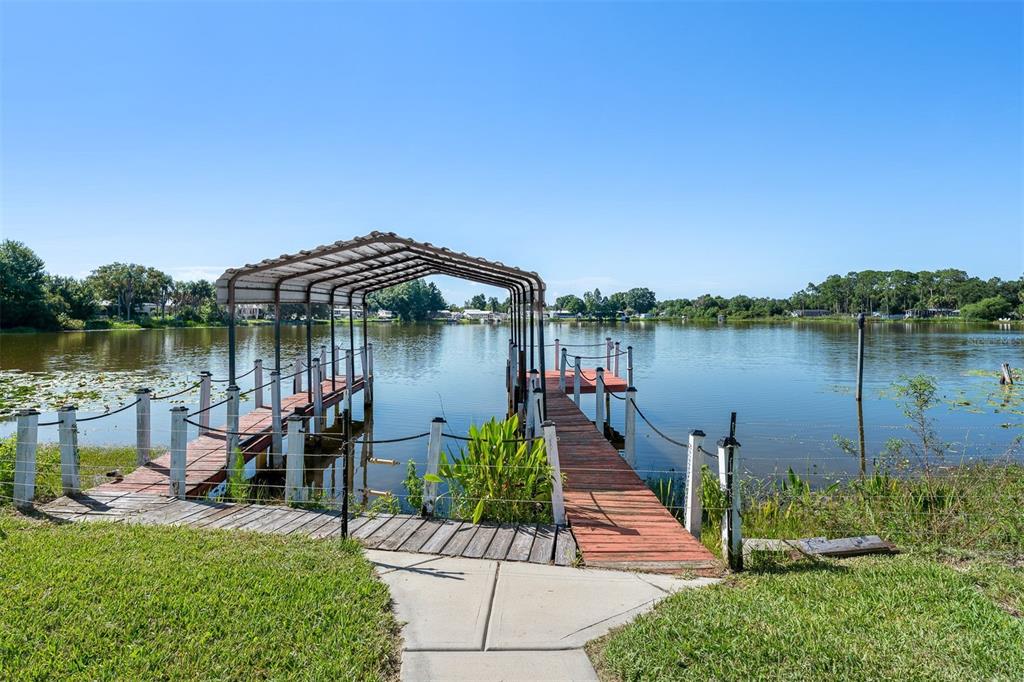 A wooden dock with a metal roof extends into a calm lake from a grassy yard — 2008 LAKE ELLEN DRIVE, HAINES CITY, FL