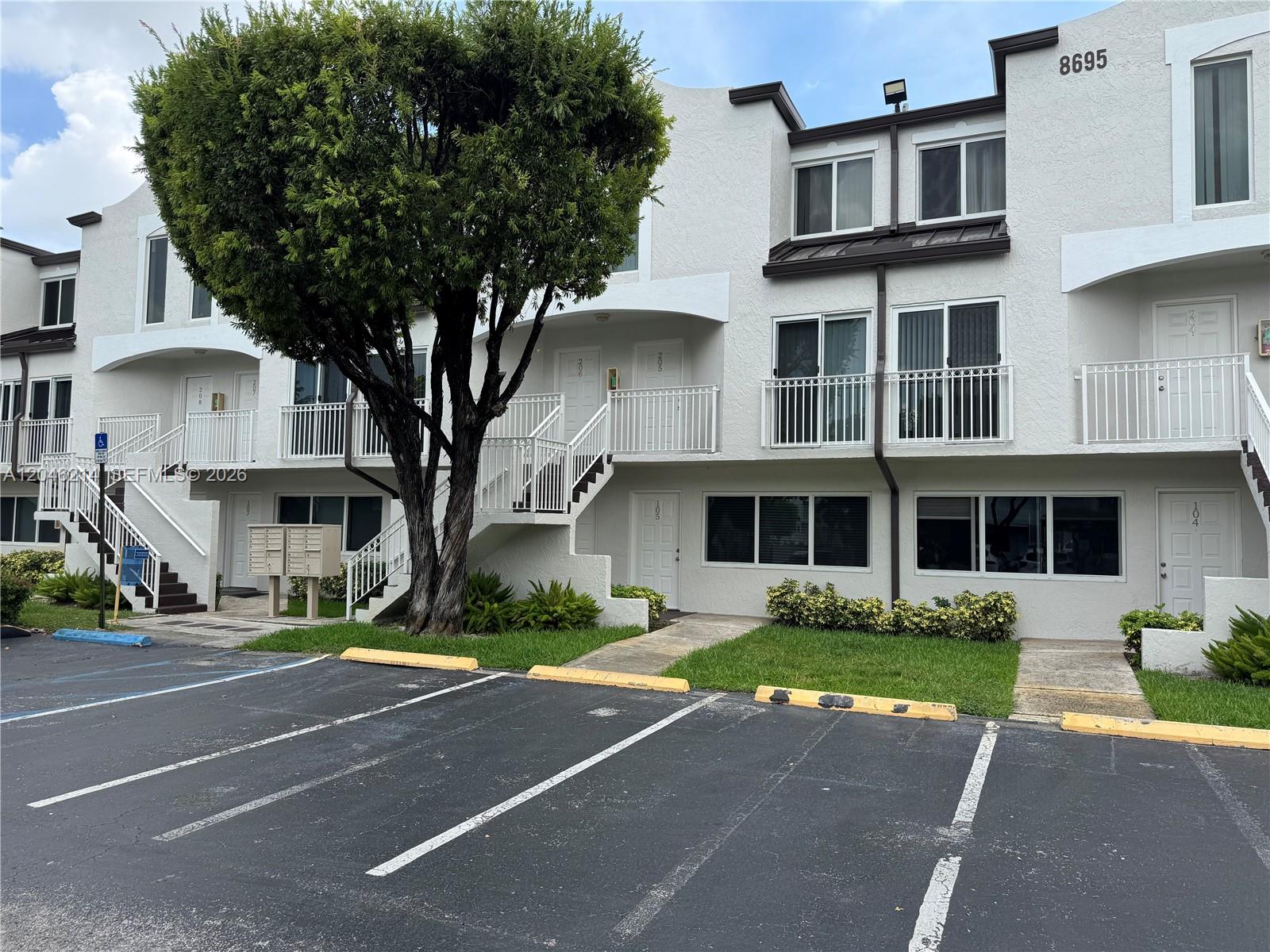 A multi-story residential building features white stucco walls, balconies, and a large tree in front — 8695 NW 6th Ln # 105, Miami FL 33126, MIAMI, FL