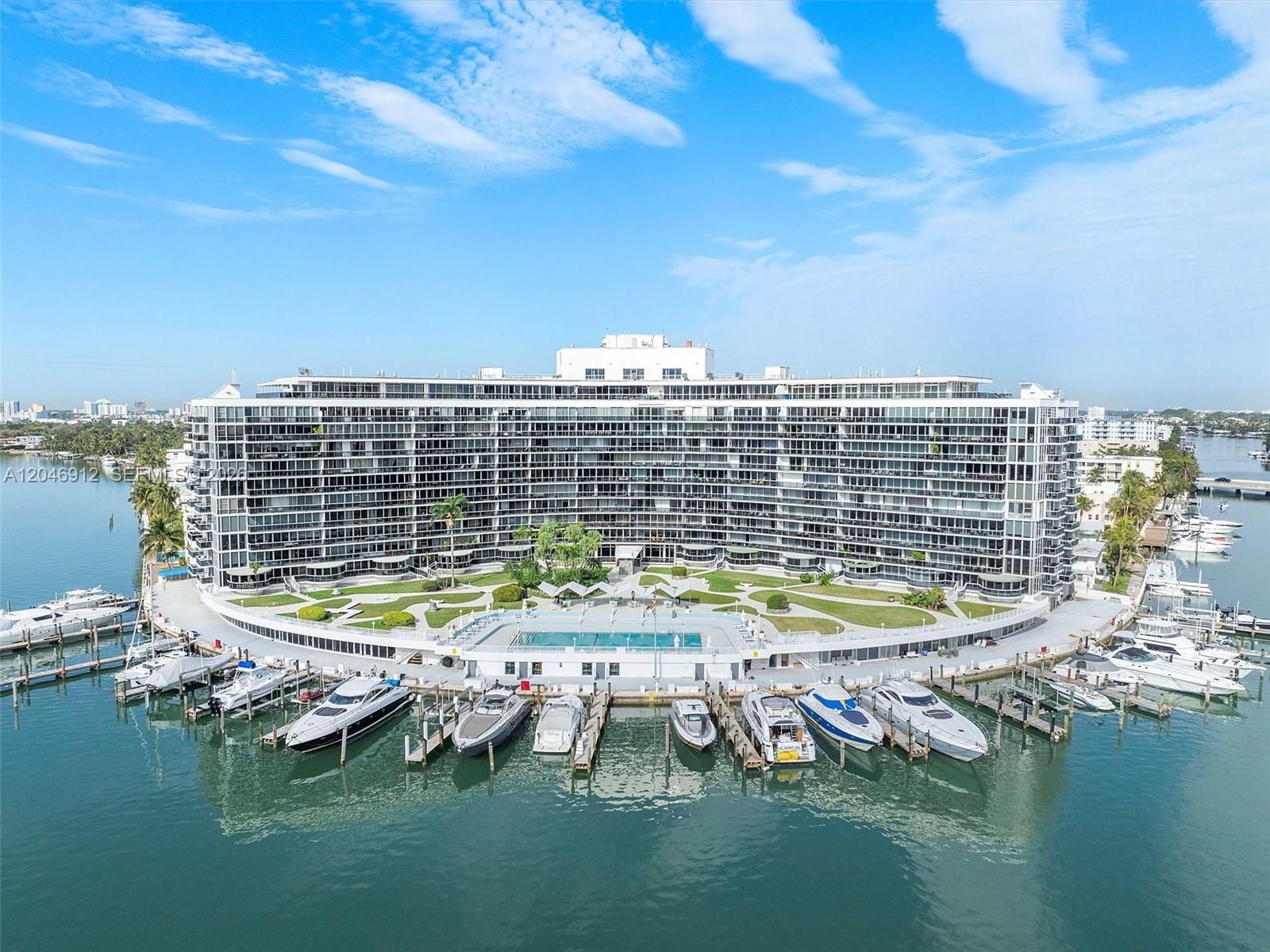 An aerial view of a curved waterfront apartment building with a pool and boat docks — 900 Bay Dr # 527, Miami Beach FL 33141, MIAMI BEACH, FL