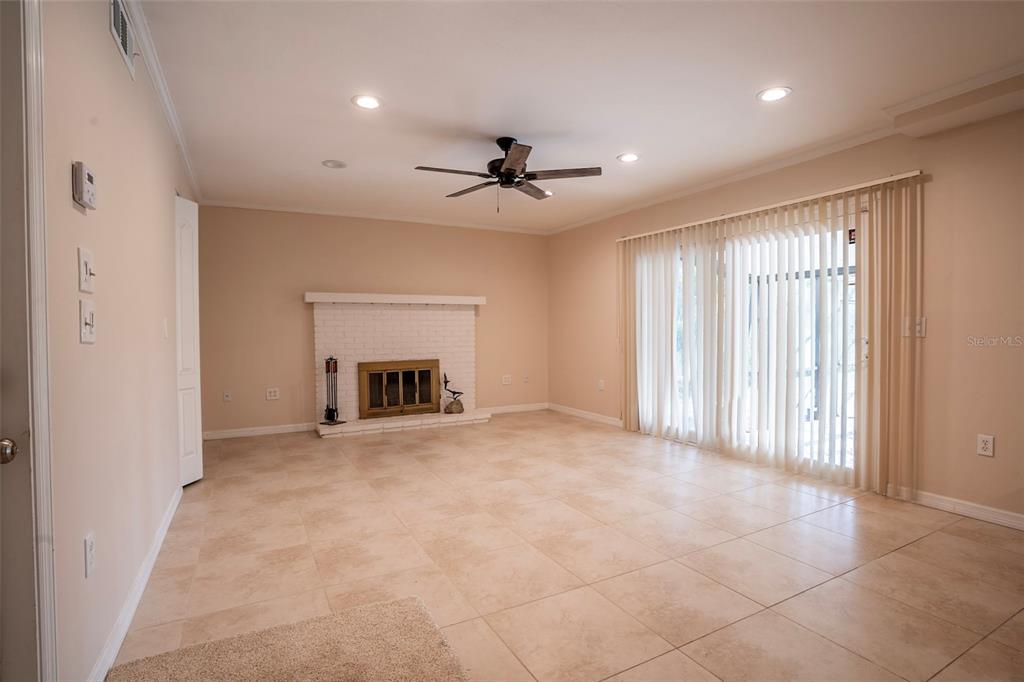 A living room features beige tile flooring, a white brick fireplace, and floor-to-ceiling vertical blinds — 7324 PHILLIPS STREET, SARASOTA, FL