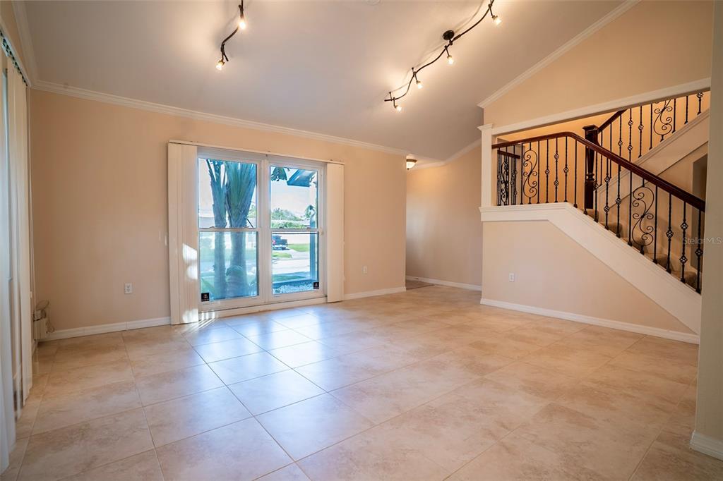 A bright living room features light tile flooring, a staircase with iron railings, and sliding doors — 7324 PHILLIPS STREET, SARASOTA, FL