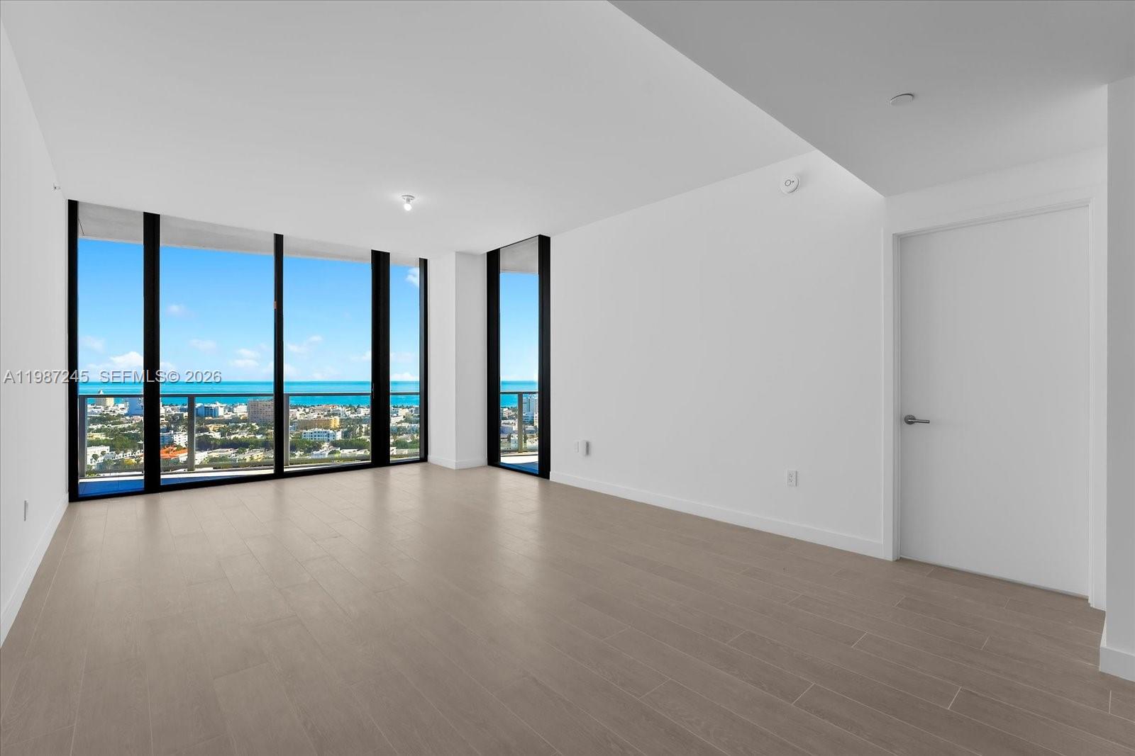An empty room with light wood floors, white walls, and floor-to-ceiling windows overlooking the ocean — 500 Alton Rd # 2402, Miami Beach FL 33139, MIAMI BEACH, FL
