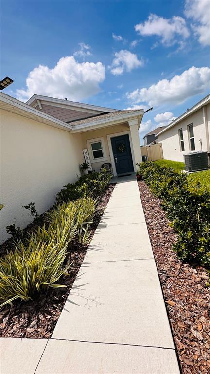 A concrete walkway leads to the front entrance of a house with a blue door — 4260 PEBBLES THROW DRIVE, KISSIMMEE, FL