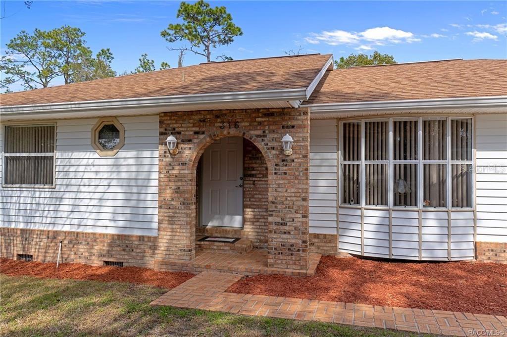 A single-story house exterior features white horizontal siding, a brick arched entryway, and bay windows — 316 PEONY STREET, INVERNESS, FL