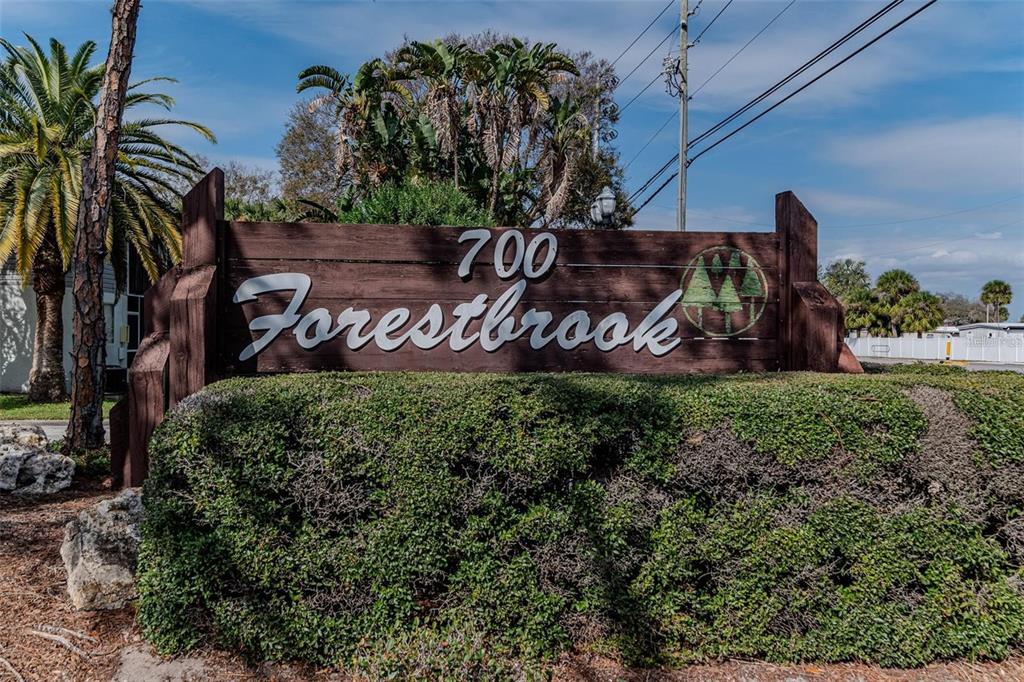 A wooden sign for Forestbrook stands behind a large green hedge under a blue sky — 700 STARKEY ROAD UNIT 1114, LARGO, FL