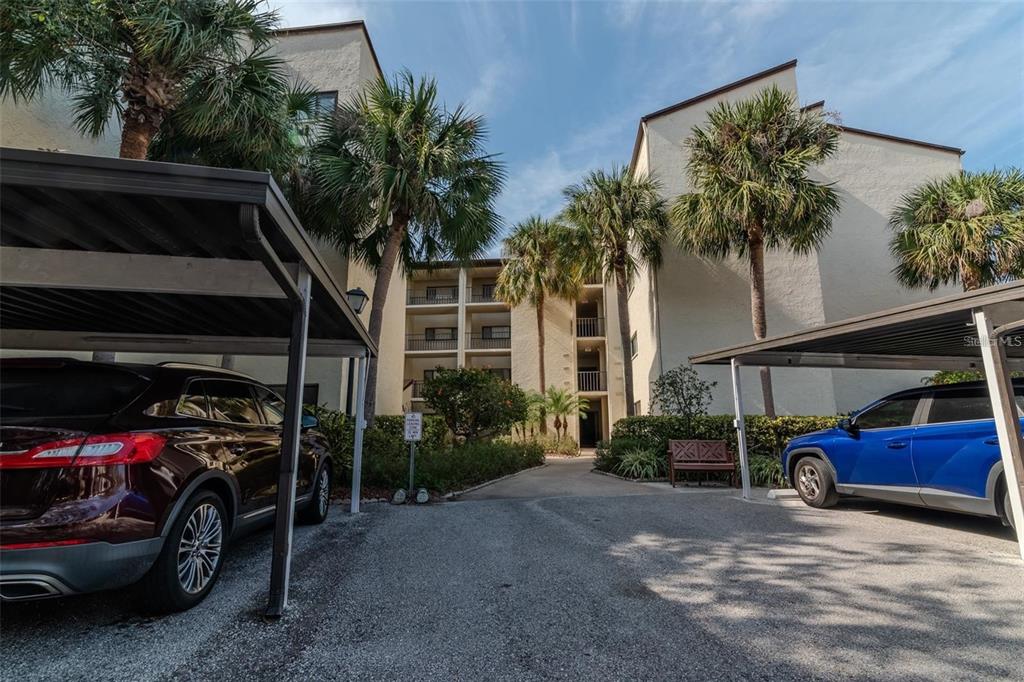A multi-story apartment building exterior with covered parking spaces and palm trees in the foreground — 700 STARKEY ROAD UNIT 1114, LARGO, FL