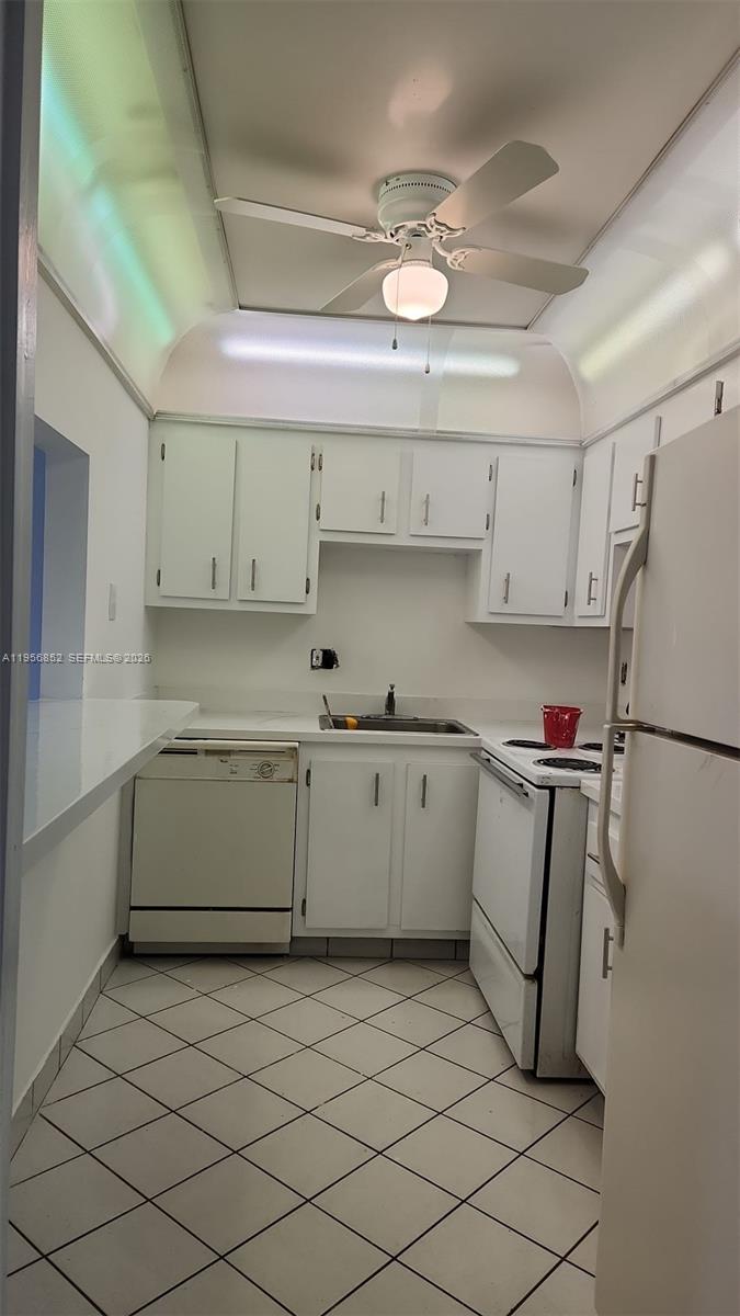 A galley kitchen features white cabinets, white appliances, and light-colored tile flooring — 4174 Inverrary Dr # 311, Lauderhill FL 33319, LAUDERHILL, FL