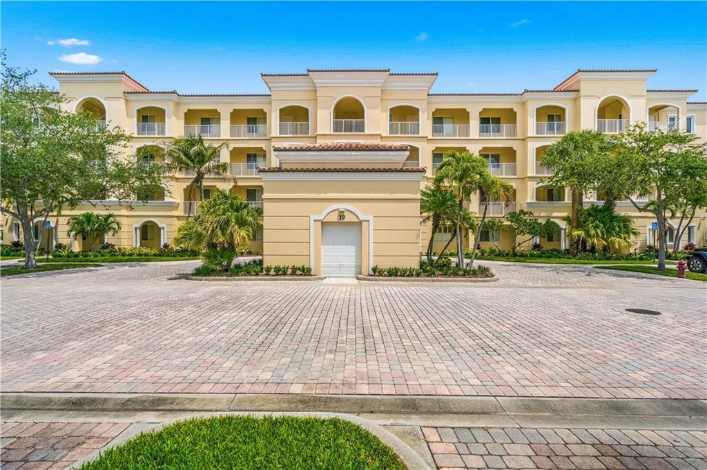 A multi-story beige apartment building with a central garage entrance and paved driveway — HUTCHINSON ISLAND, FL