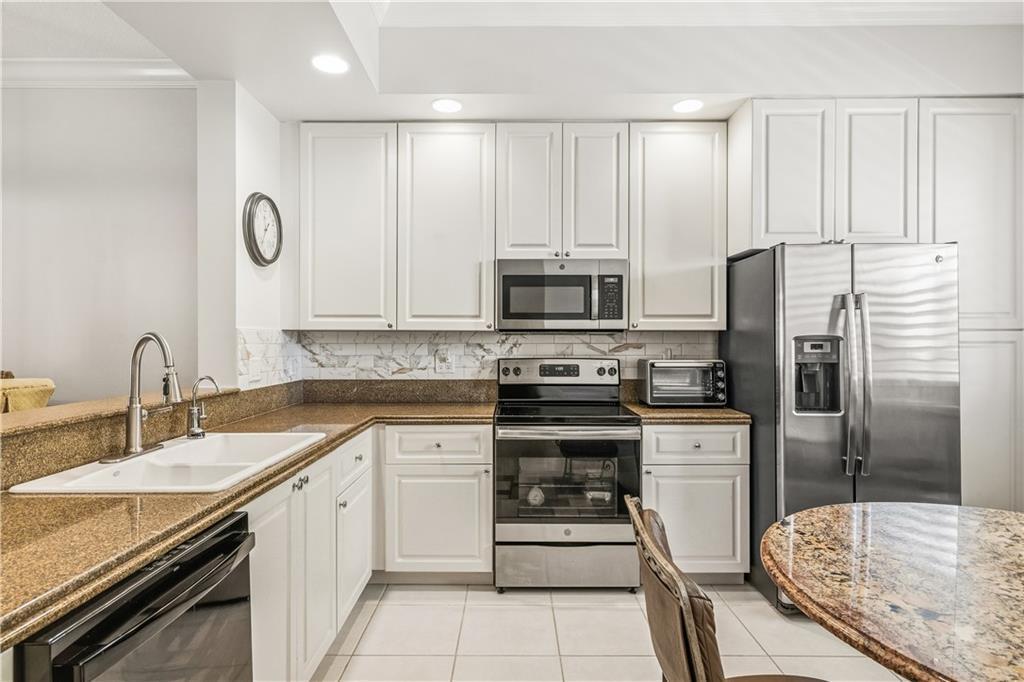 A kitchen features white cabinets, granite countertops, stainless steel appliances, and a tile backsplash — HUTCHINSON ISLAND, FL
