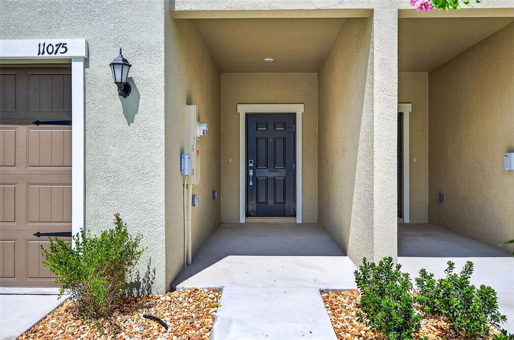 A tan stucco exterior features a dark front door, a garage, and a concrete walkway — 11075 65TH TERRACE E, PALMETTO, FL