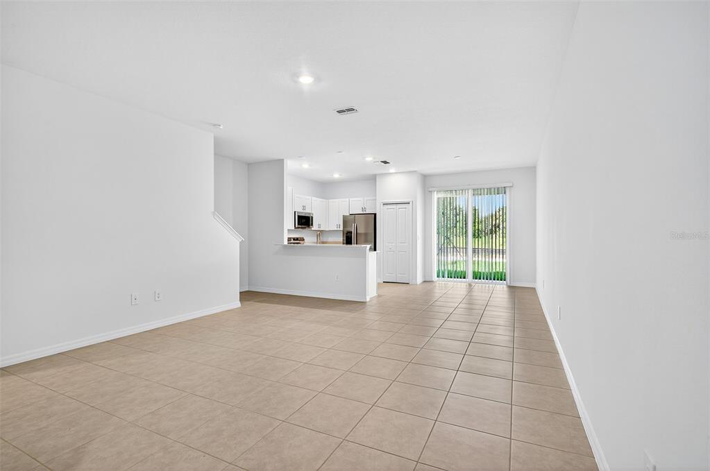 An open-concept living area with tile flooring leads to a kitchen and sliding glass doors — 11075 65TH TERRACE E, PALMETTO, FL