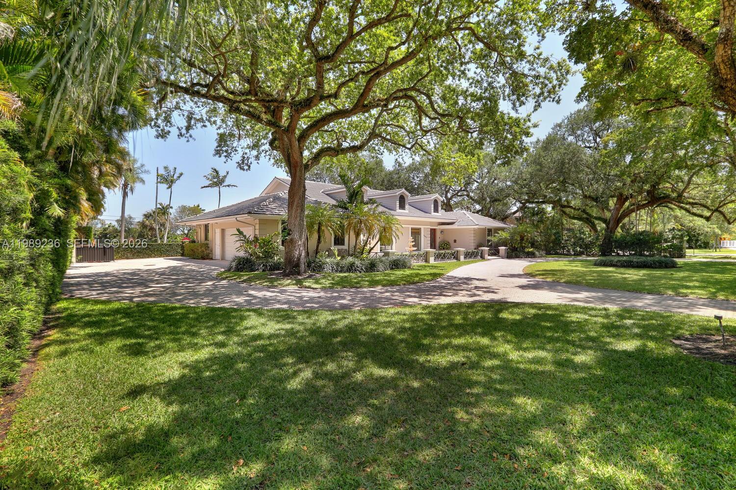 A single-story house with a circular paver driveway sits under large, mature oak trees — 3425 Alhambra Cir, Coral Gables FL 33134, CORAL GABLES, FL