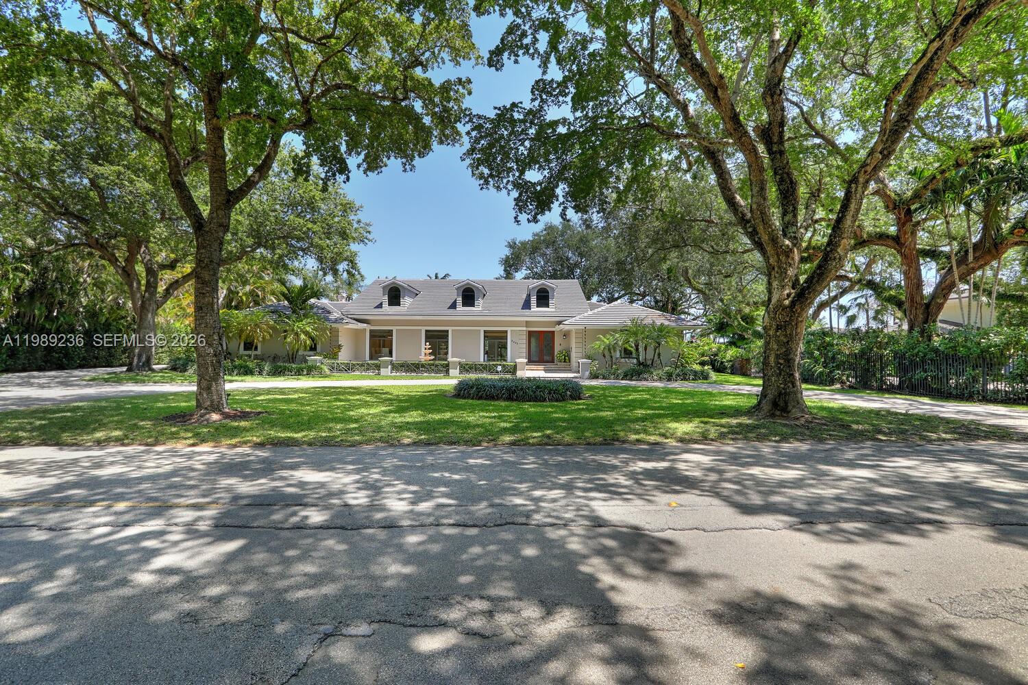 A single-story house with a gray roof and dormer windows sits behind a large lawn — 3425 Alhambra Cir, Coral Gables FL 33134, CORAL GABLES, FL