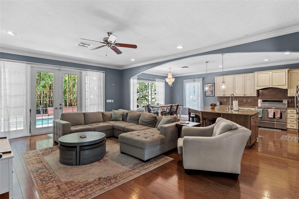An open-concept living room features a sectional sofa, hardwood floors, and an adjacent kitchen — 3317 W LEONA STREET, TAMPA, FL
