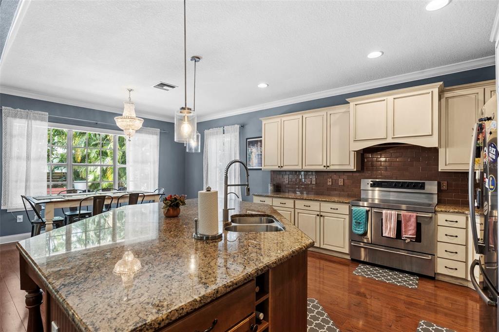 A kitchen features granite countertops, cream-colored cabinets, a stainless steel stove, and a dining area — 3317 W LEONA STREET, TAMPA, FL