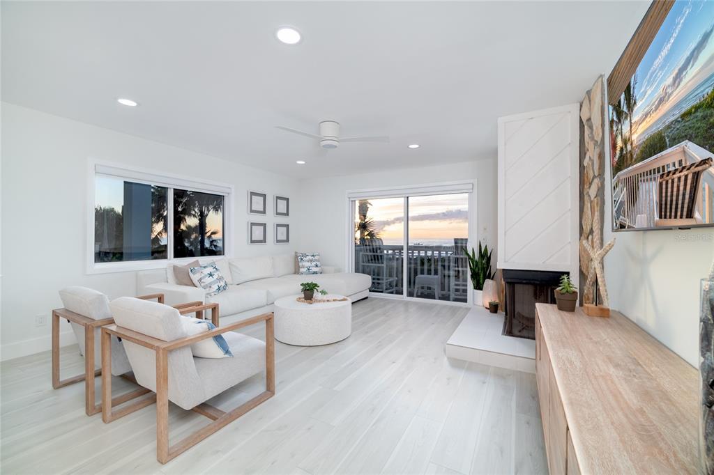 A bright living room features white walls, light wood flooring, a fireplace, and ocean views — 1104 BEACH TRAIL UNIT 1, INDIAN ROCKS BEACH, FL