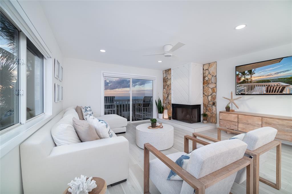 A bright living room features a stone fireplace, white sofa, two armchairs, and ocean views — 1104 BEACH TRAIL UNIT 1, INDIAN ROCKS BEACH, FL