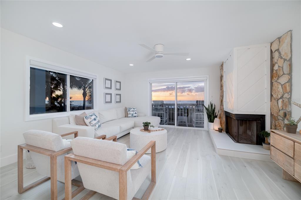 A bright living room features a white sectional, two armchairs, and a stone fireplace — 1104 BEACH TRAIL UNIT 1, INDIAN ROCKS BEACH, FL