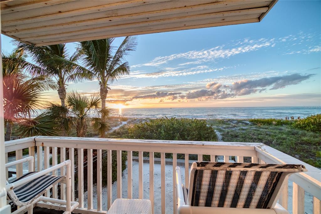 A balcony with two chairs overlooks a sandy beach and the ocean at sunset — 1104 BEACH TRAIL UNIT 1, INDIAN ROCKS BEACH, FL