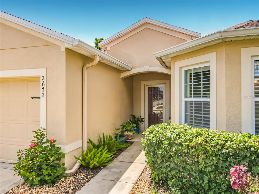 The exterior of a beige house features a front entrance, a garage, and landscaping — 2672 STAR CORAL LANE, NEW SMYRNA BEACH, FL