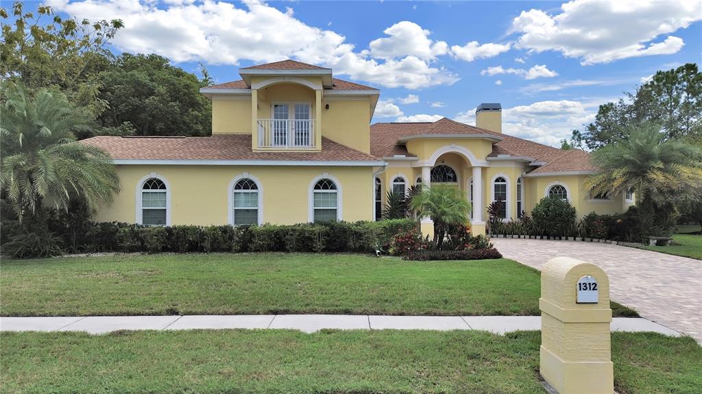 A yellow two-story house with a paved driveway, arched windows, and a front balcony — 1312 FISHING LAKE DRIVE, ODESSA, FL