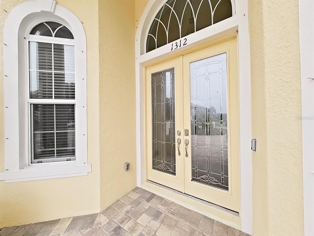 A light yellow exterior wall features a double front door with glass inserts and windows — 1312 FISHING LAKE DRIVE, ODESSA, FL
