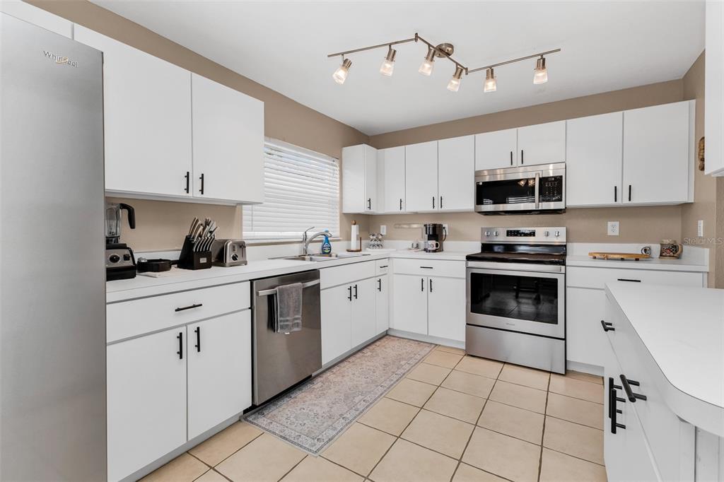 A kitchen with white cabinets, stainless steel appliances, and tile flooring — 24208 BUCKINGHAM WAY, PUNTA GORDA, FL