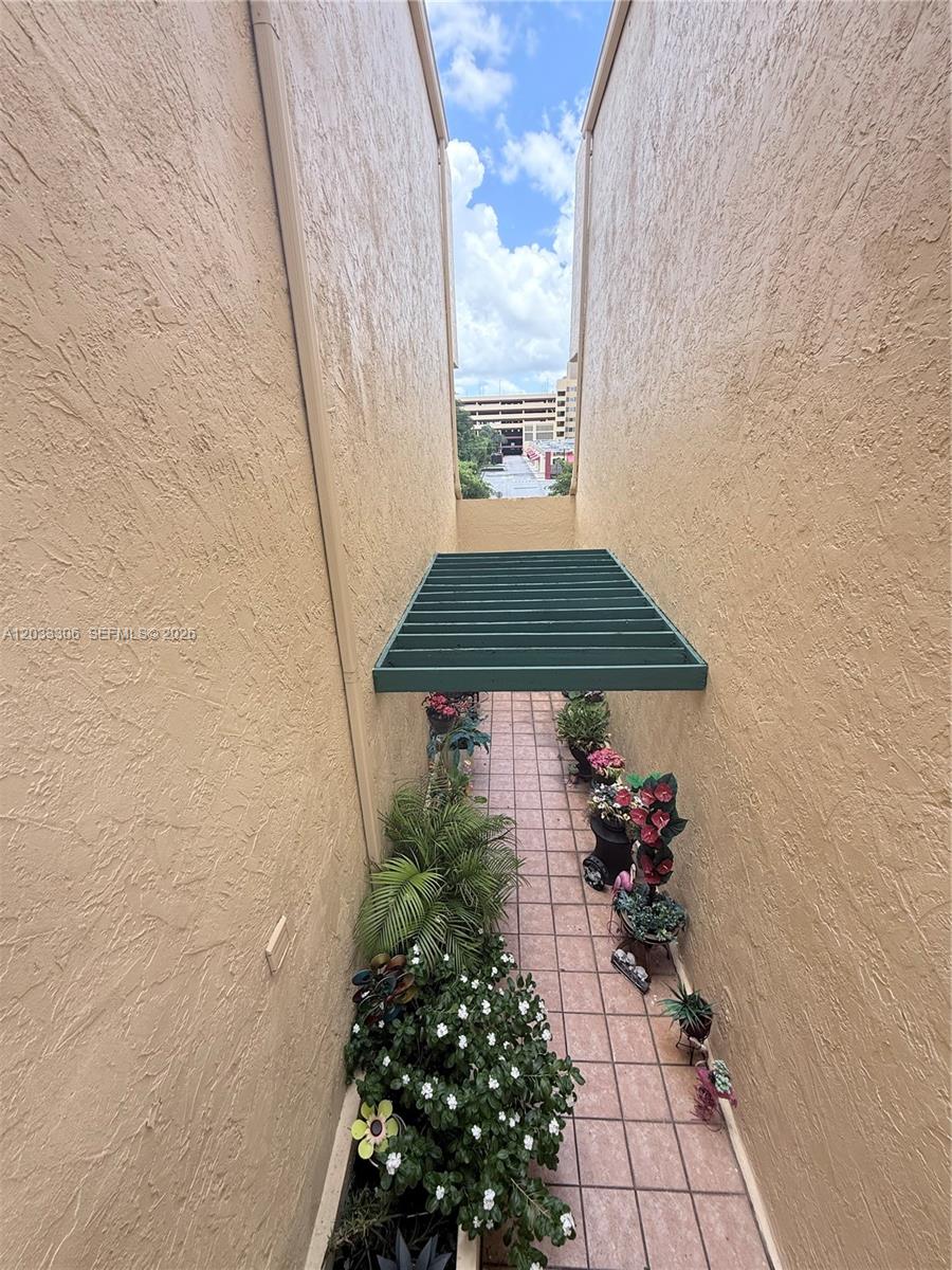 A narrow outdoor walkway between two beige stucco walls features potted plants and a trellis — 1975 W 44th Pl # 401, Hialeah FL 33012, HIALEAH, FL