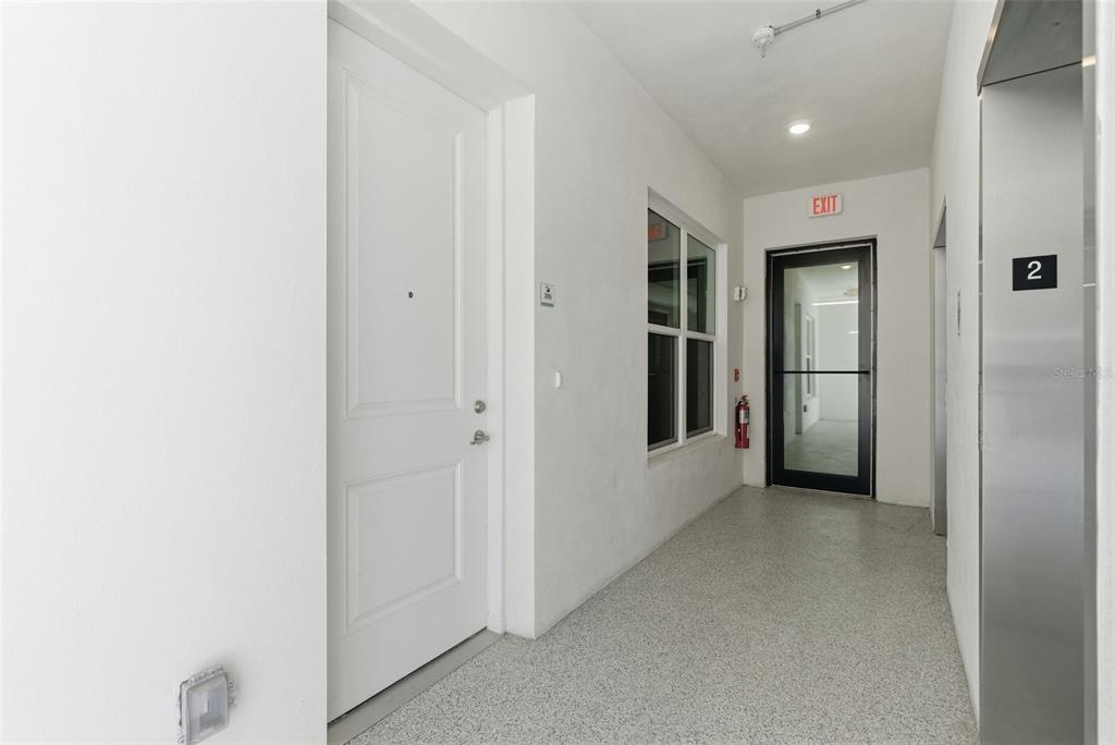 A hallway features a white door, an exit door, and a stainless steel elevator door — 400 150TH AVENUE UNIT 205, MADEIRA BEACH, FL