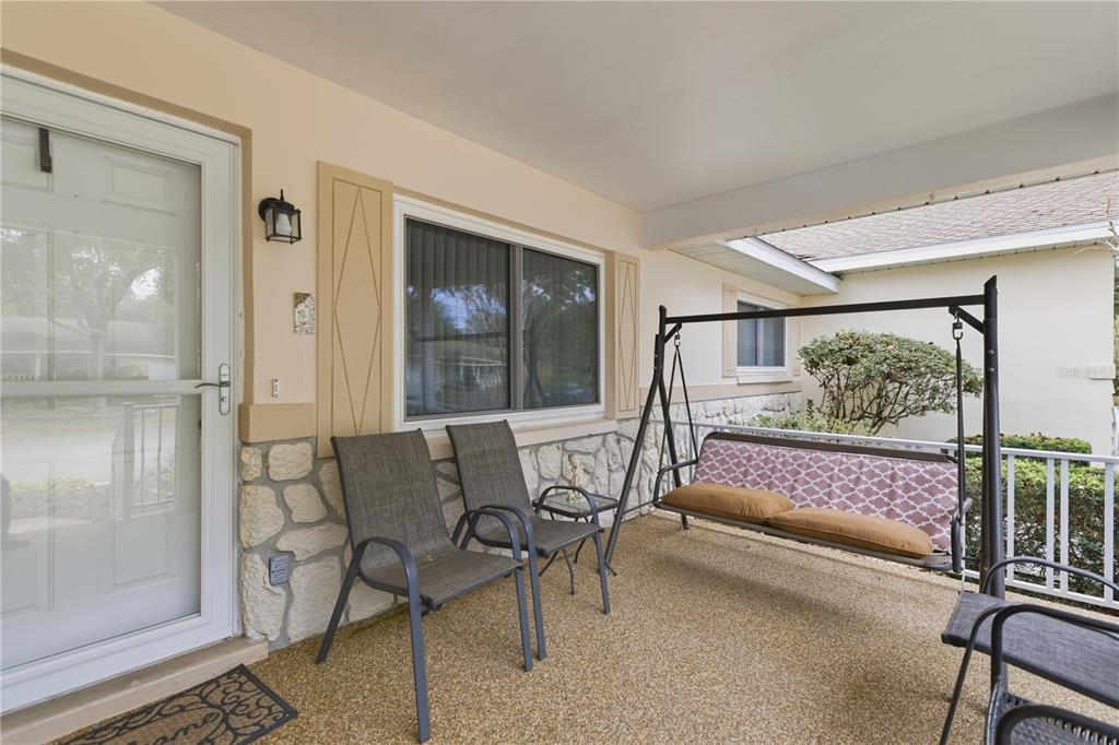 A covered porch features a stone facade, two chairs, and a hanging swing bench — 8702 SW 94TH STREET UNIT E, OCALA, FL