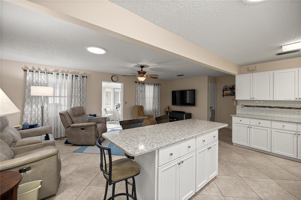 An open-concept kitchen and living area features white cabinets, granite countertops, and tile flooring — 8702 SW 94TH STREET UNIT E, OCALA, FL
