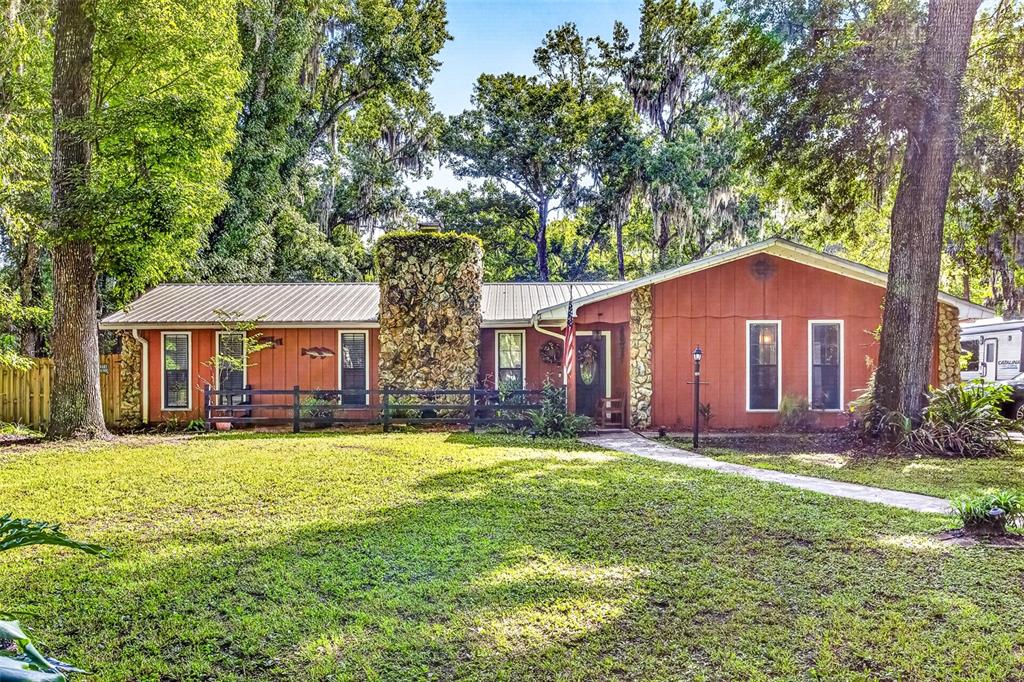 A single-story house with red siding, a stone chimney, and a metal roof among trees — 625 WILDWOOD DRIVE, NEW SMYRNA BEACH, FL