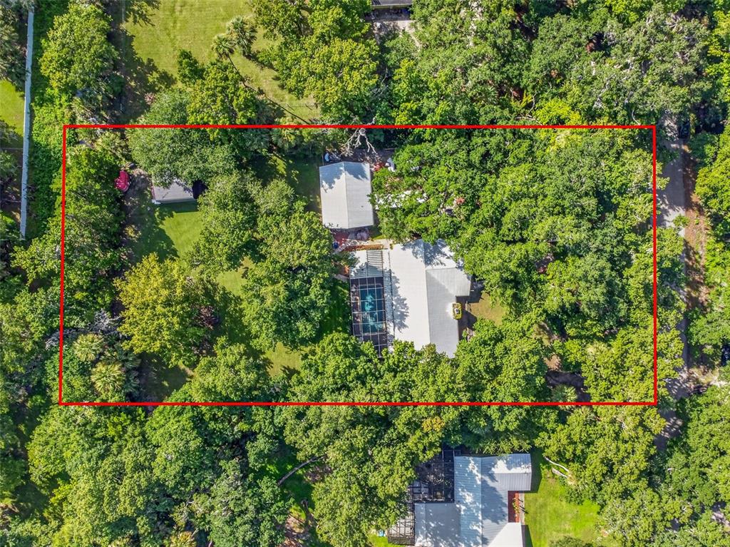 An aerial view shows a house with a pool and detached garage surrounded by trees — 625 WILDWOOD DRIVE, NEW SMYRNA BEACH, FL