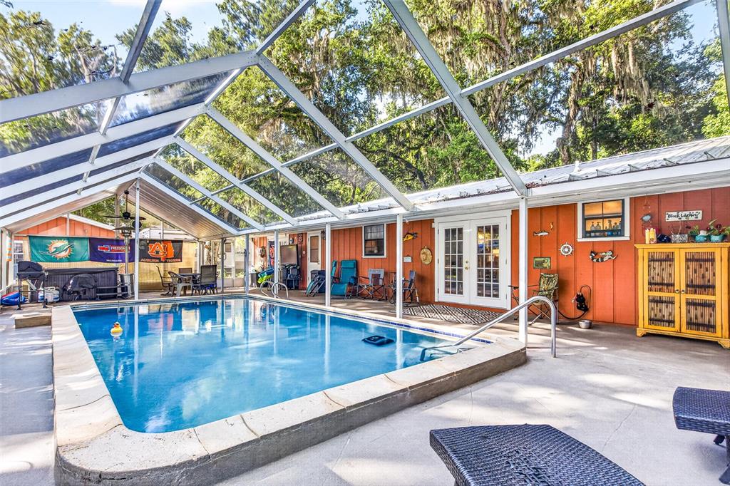 A screened-in swimming pool sits on a concrete patio next to an orange-sided house — 625 WILDWOOD DRIVE, NEW SMYRNA BEACH, FL