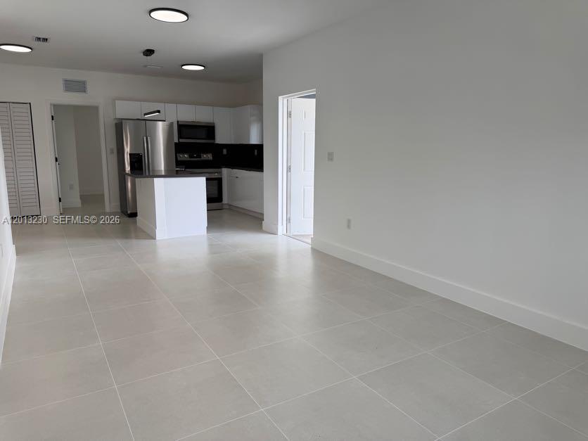 A modern kitchen with stainless steel appliances and white cabinets opens to a tiled living area — 1440 NW 61st St # 2, Miami FL 33142, MIAMI, FL
