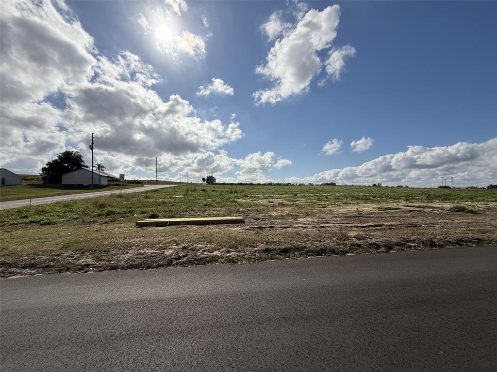 A vacant, grassy lot sits alongside an asphalt road under a bright, cloudy sky — 203 SEMINOLE BEACH DRIVE, BABSON PARK, FL