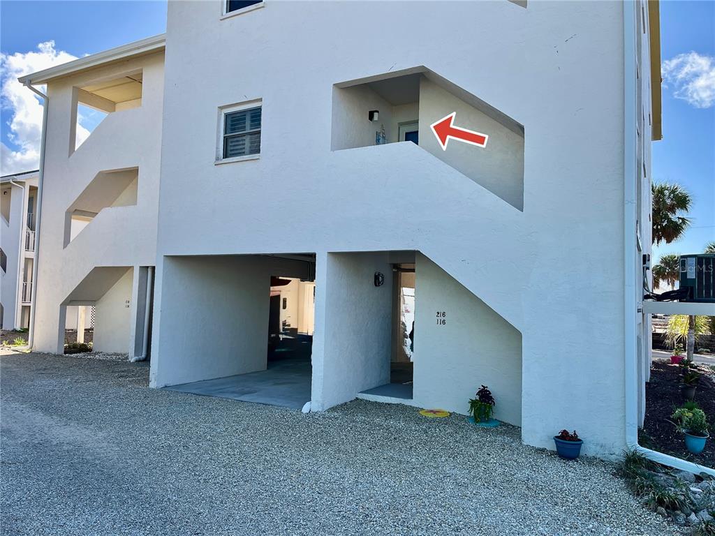 An exterior view of a multi-story building with a gravel driveway and an arrow pointing upward — 5031 N BEACH ROAD UNIT 116, ENGLEWOOD, FL