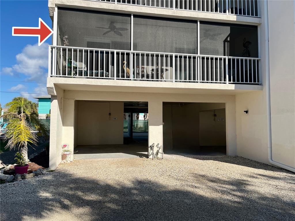 A screened-in balcony sits above a ground-level parking area with a gravel driveway — 5031 N BEACH ROAD UNIT 116, ENGLEWOOD, FL