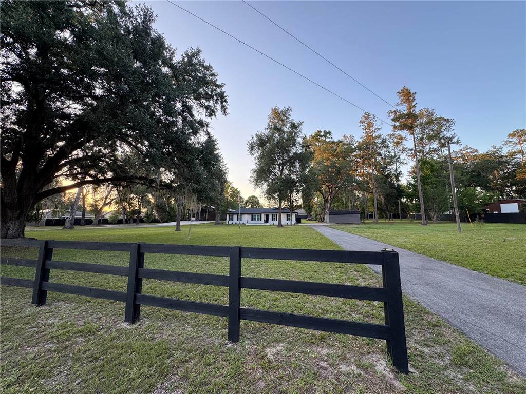 A white house sits at the end of a long driveway behind a black fence — 6133 SE 123RD LANE, BELLEVIEW, FL