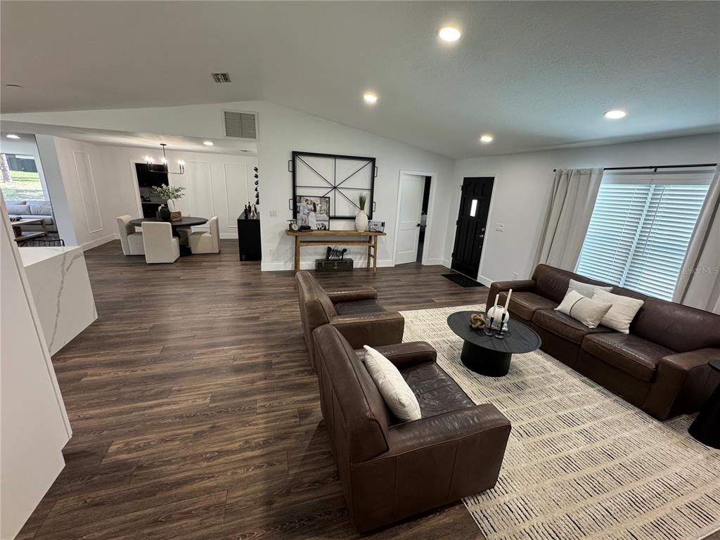 A living room with dark wood floors, leather furniture, and an adjacent dining area — 6133 SE 123RD LANE, BELLEVIEW, FL