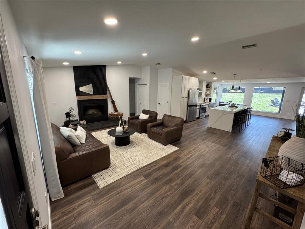An open-concept living room and kitchen featuring dark wood flooring and a black fireplace — 6133 SE 123RD LANE, BELLEVIEW, FL