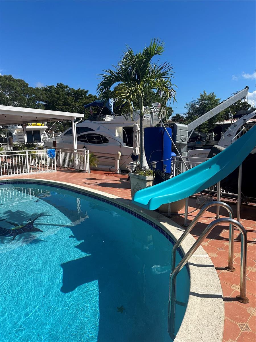 A swimming pool with a blue slide sits on a patio next to a docked yacht — 12941 Auralia Rd, North Miami FL 33181, NORTH MIAMI, FL