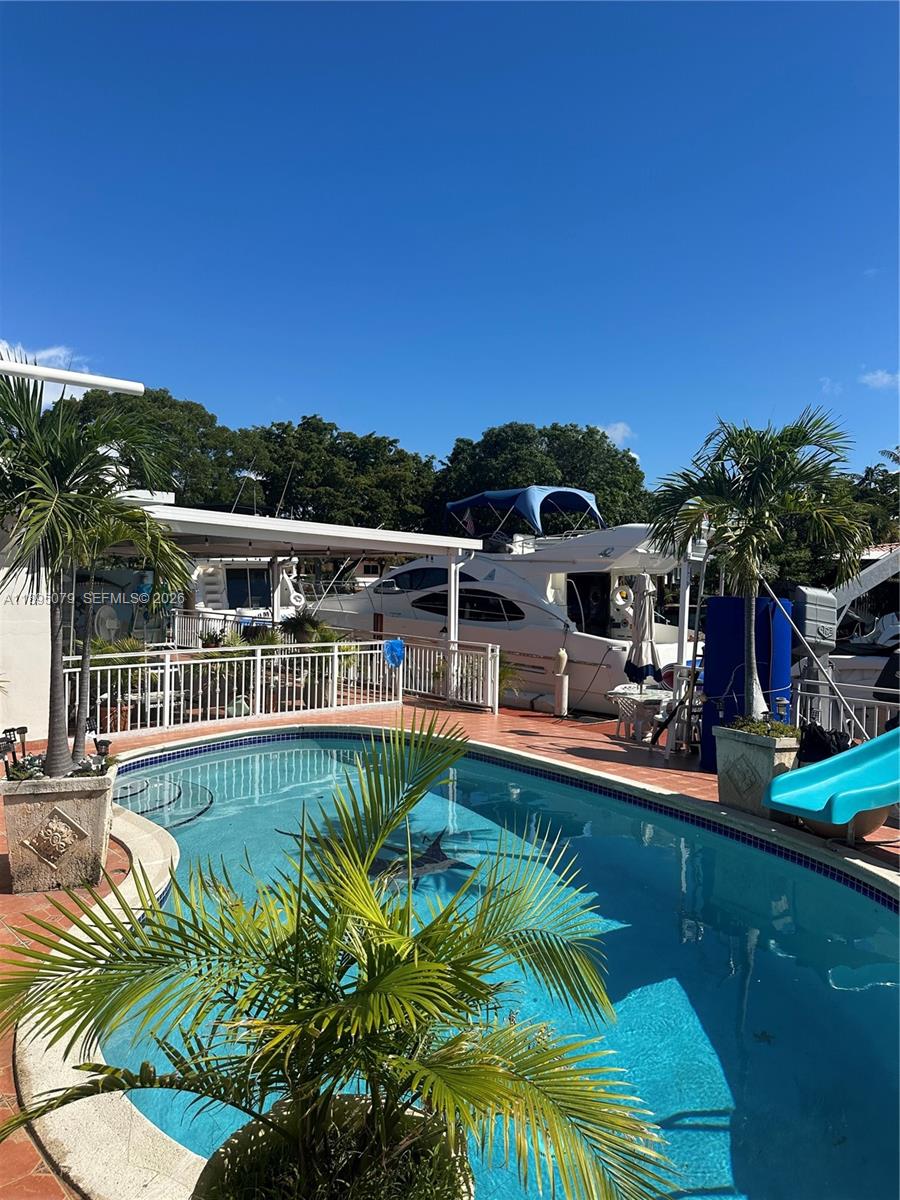 A swimming pool with a blue slide sits on a patio next to a yacht — 12941 Auralia Rd, North Miami FL 33181, NORTH MIAMI, FL