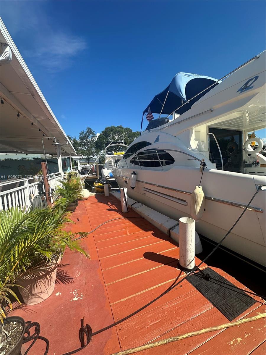 A white yacht is docked alongside a wooden pier with potted plants — 12941 Auralia Rd, North Miami FL 33181, NORTH MIAMI, FL
