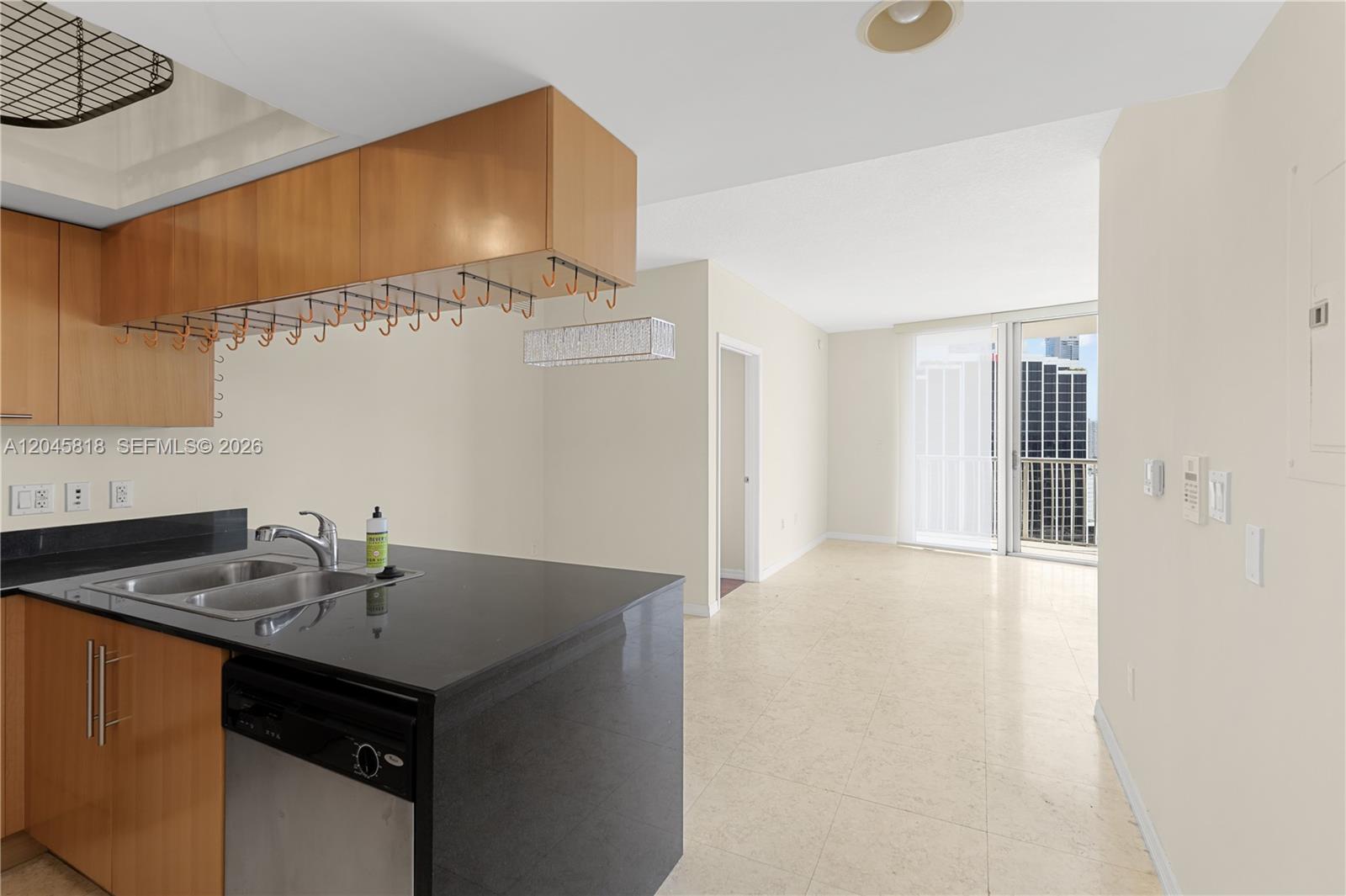 A kitchen with black countertops and wood cabinets overlooks an open living area with balcony — 1750 N Bayshore Dr # 2414, Miami FL 33132, MIAMI, FL