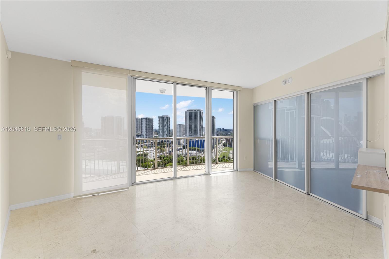 An empty room with light tile flooring, sliding glass doors, and a balcony overlooking city buildings — 1750 N Bayshore Dr # 2414, Miami FL 33132, MIAMI, FL