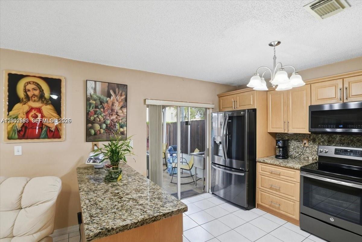 A kitchen features light wood cabinets, granite countertops, stainless steel appliances, and a sliding door — 13741 SW 160th Ter # 0, Miami FL 33177, MIAMI, FL
