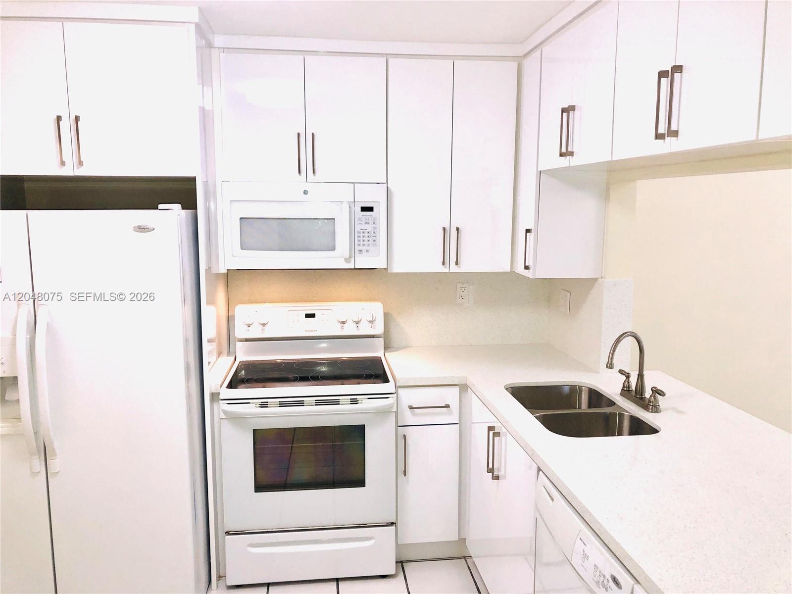 A white kitchen features a refrigerator, electric stove, microwave, and double-basin sink with countertops — 7830 Camino Real # K310, Miami FL 33143, MIAMI, FL