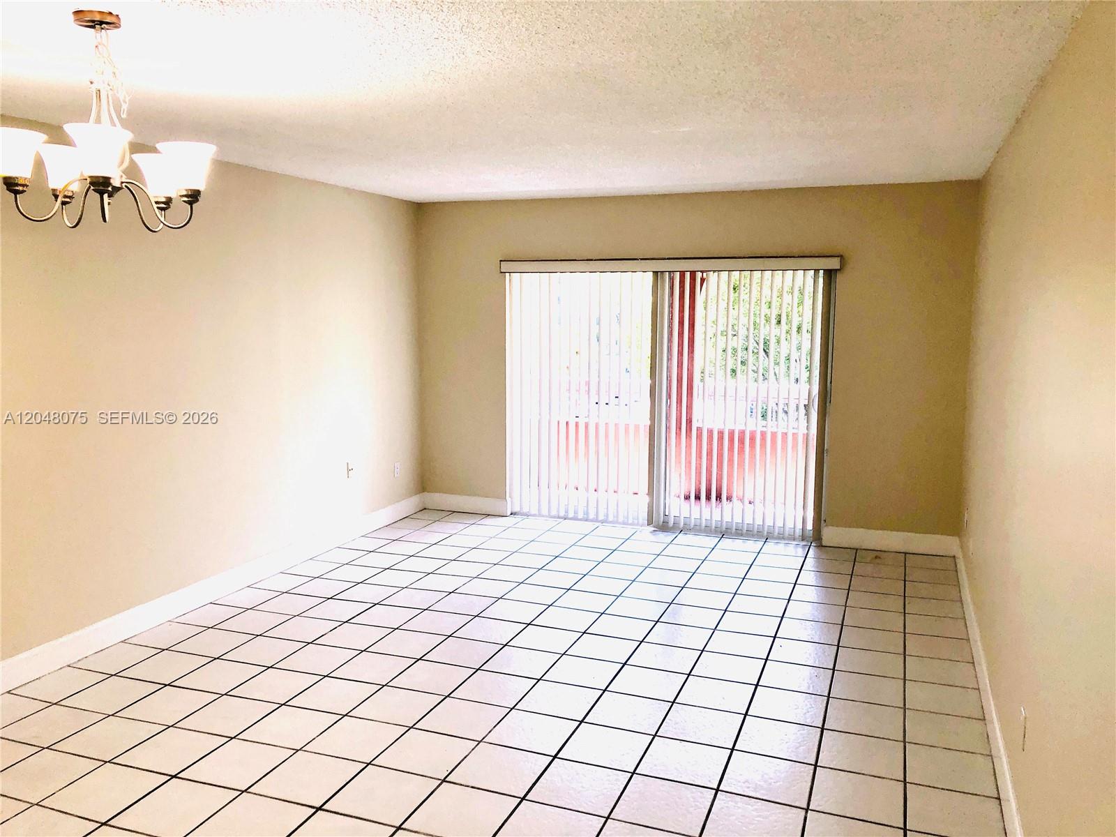 A dining room features white tiled floors, beige walls, a chandelier, and sliding glass doors — 7830 Camino Real # K310, Miami FL 33143, MIAMI, FL